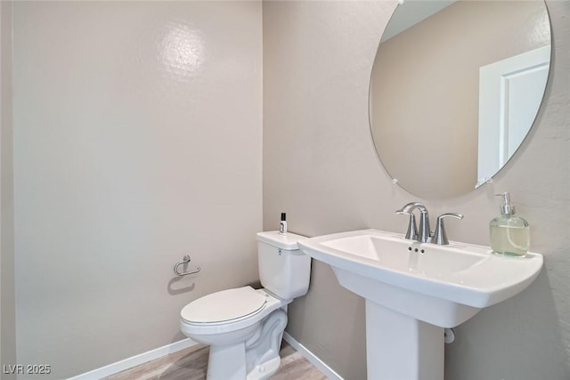 half bathroom featuring a sink, baseboards, toilet, and wood finished floors