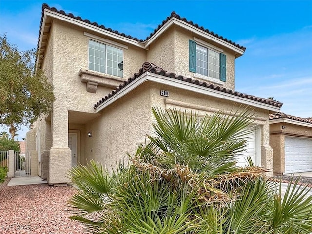 mediterranean / spanish-style home with a tiled roof, a gate, a garage, and stucco siding