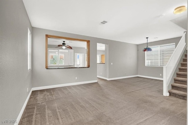 unfurnished living room with stairway, carpet flooring, a ceiling fan, and baseboards