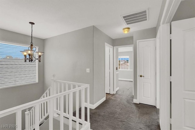 corridor with visible vents, baseboards, an upstairs landing, a notable chandelier, and dark colored carpet