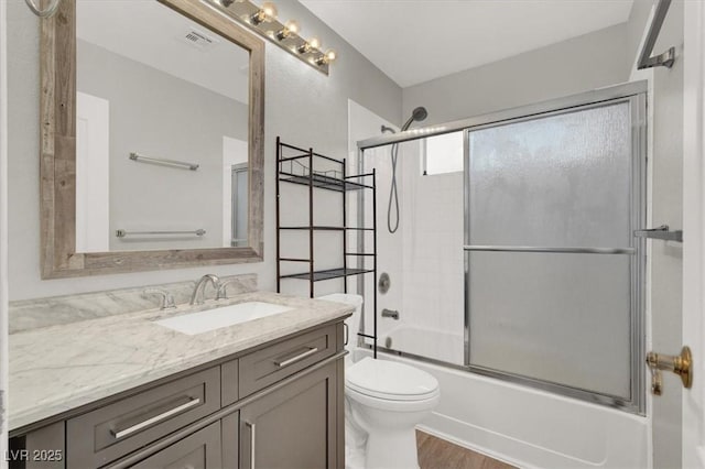 bathroom with visible vents, toilet, wood finished floors, bath / shower combo with glass door, and vanity