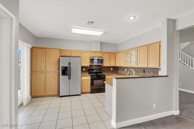 kitchen with stainless steel appliances, backsplash, light brown cabinets, and dark stone counters