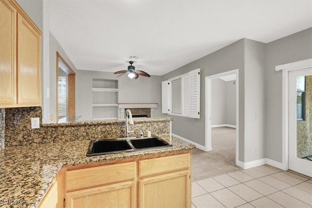 kitchen featuring light brown cabinets, a peninsula, ceiling fan, and a sink