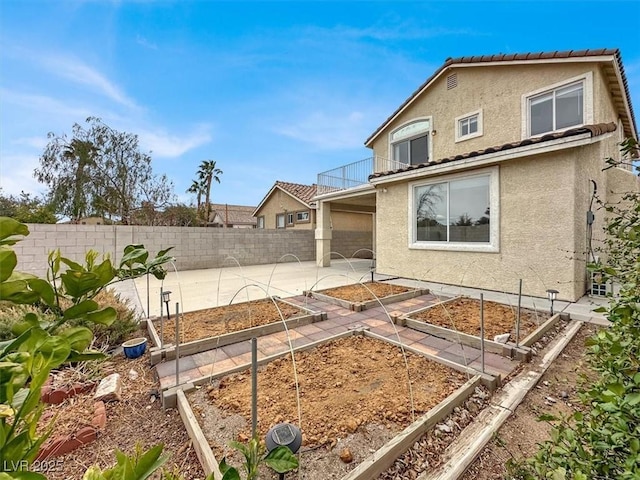 rear view of property with a vegetable garden, a fenced backyard, stucco siding, a tiled roof, and a patio area