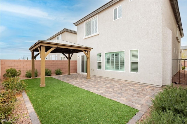 rear view of property featuring a gazebo, stucco siding, a lawn, and fence