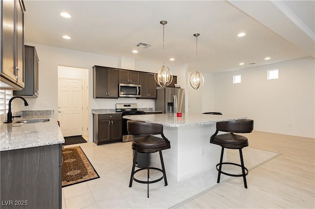 kitchen featuring a kitchen bar, visible vents, a sink, stainless steel appliances, and dark brown cabinets