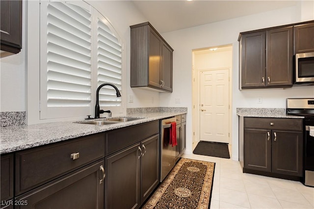 kitchen featuring dark brown cabinets, light stone countertops, light tile patterned floors, stainless steel appliances, and a sink