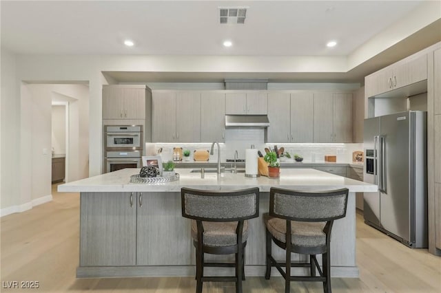 kitchen with visible vents, backsplash, under cabinet range hood, appliances with stainless steel finishes, and a sink