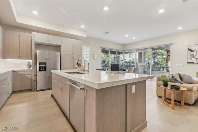 kitchen featuring open floor plan, an island with sink, decorative backsplash, appliances with stainless steel finishes, and a sink