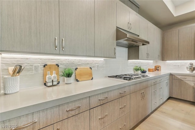 kitchen featuring light countertops, stainless steel gas stovetop, tasteful backsplash, and under cabinet range hood