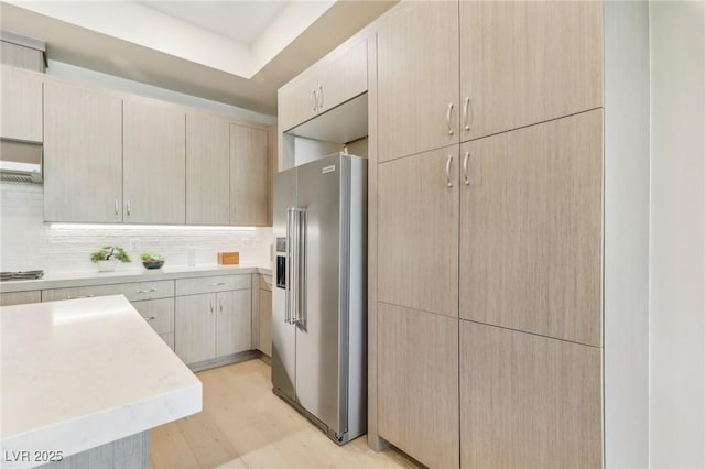 kitchen with light brown cabinetry, stainless steel appliances, light countertops, light wood-style floors, and tasteful backsplash