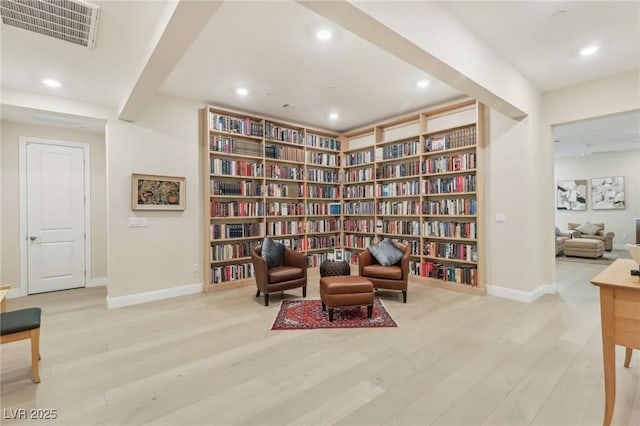 sitting room with visible vents, baseboards, wall of books, recessed lighting, and wood finished floors