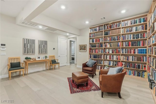 living area featuring wood finished floors, recessed lighting, wall of books, and baseboards