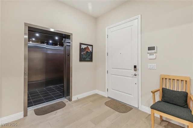 foyer with elevator, baseboards, and wood finished floors