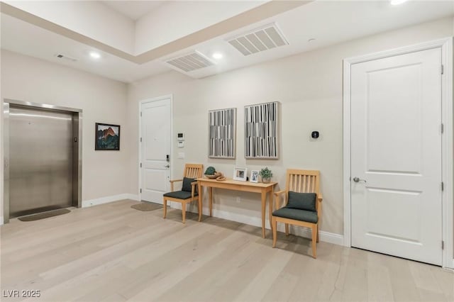 interior space with elevator, visible vents, light wood-style flooring, and baseboards