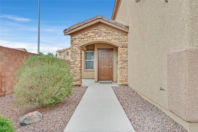 property entrance featuring stone siding, stucco siding, and fence