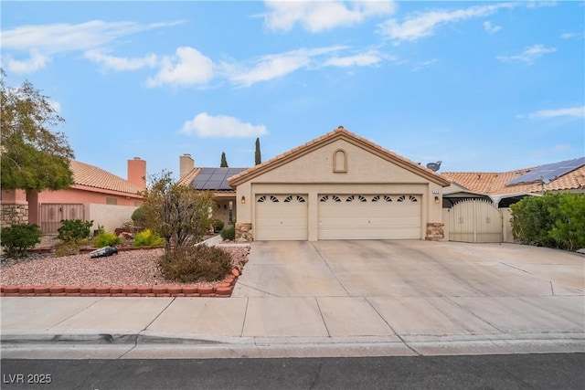 view of front of property with a gate, an attached garage, stucco siding, concrete driveway, and roof mounted solar panels