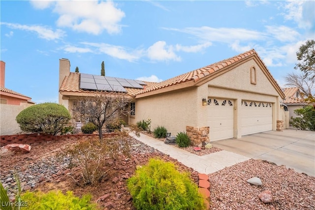 view of front facade featuring stucco siding, driveway, a tile roof, a garage, and solar panels