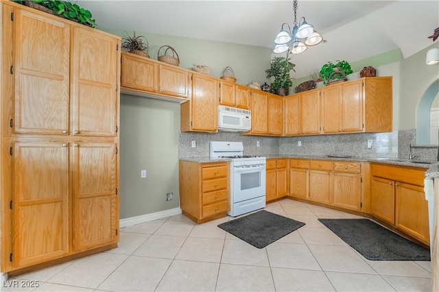 kitchen featuring light stone counters, a sink, backsplash, white appliances, and light tile patterned floors