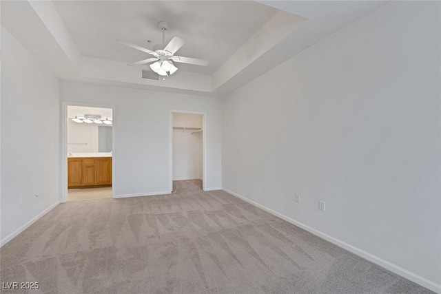 unfurnished bedroom with visible vents, a raised ceiling, baseboards, light colored carpet, and a spacious closet