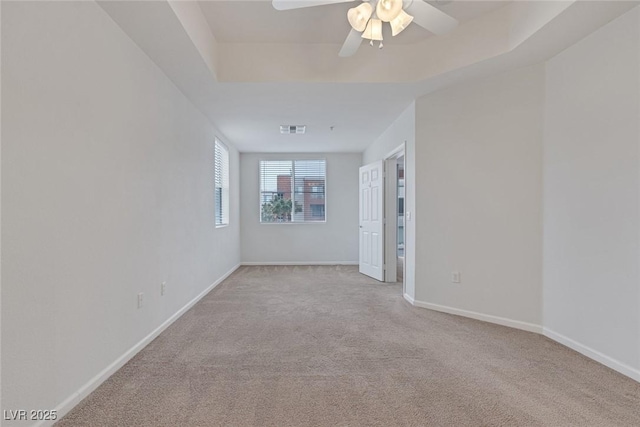 unfurnished room with visible vents, a raised ceiling, baseboards, light colored carpet, and ceiling fan