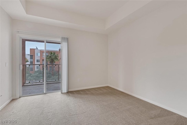 empty room with carpet flooring, a raised ceiling, and baseboards