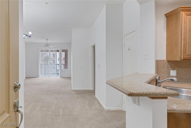 kitchen with baseboards, light stone countertops, light colored carpet, a ceiling fan, and a sink