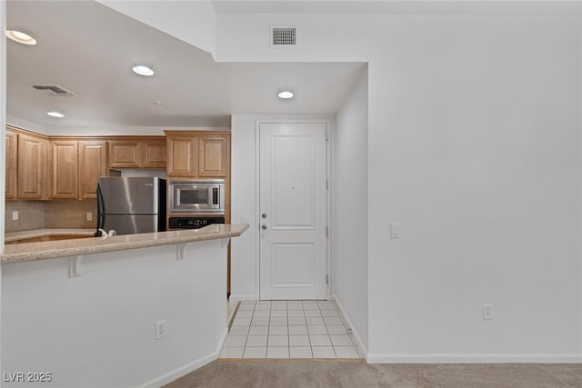 kitchen featuring stainless steel appliances, light carpet, visible vents, and a breakfast bar