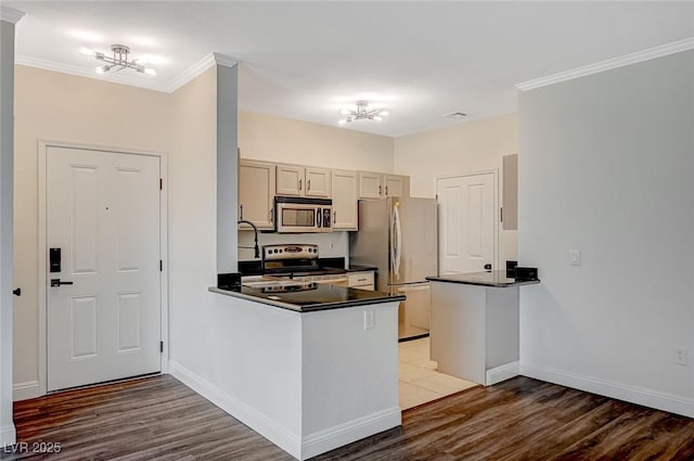 kitchen featuring dark countertops, crown molding, a peninsula, wood finished floors, and stainless steel appliances