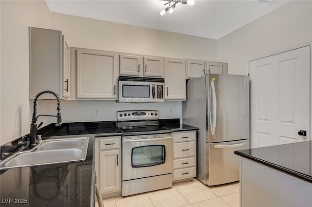 kitchen featuring dark countertops, light tile patterned floors, gray cabinets, stainless steel appliances, and a sink