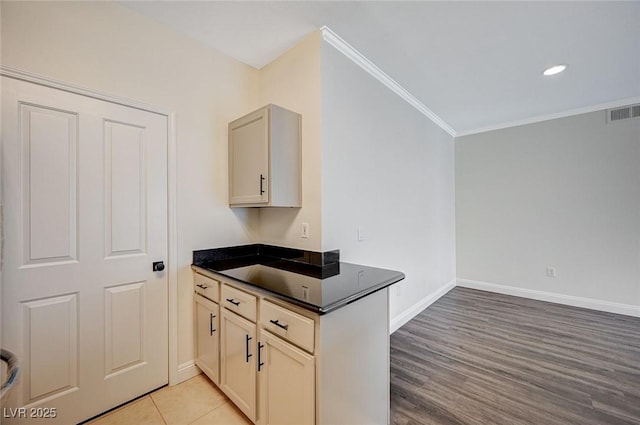 kitchen with dark countertops, visible vents, crown molding, baseboards, and light wood-style flooring