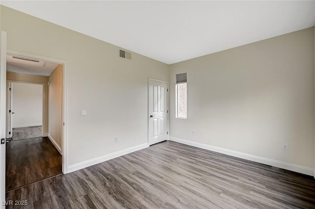 empty room featuring attic access, wood finished floors, visible vents, and baseboards