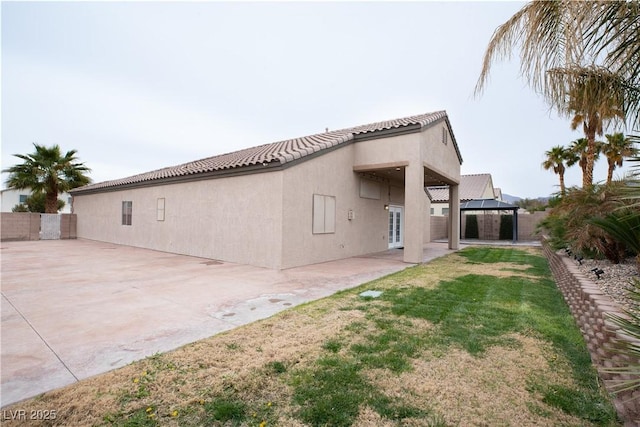 back of property with fence, stucco siding, a gazebo, a tile roof, and a patio area