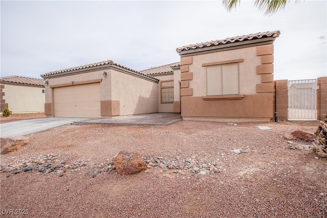 mediterranean / spanish house featuring stucco siding, a gate, a tile roof, concrete driveway, and a garage