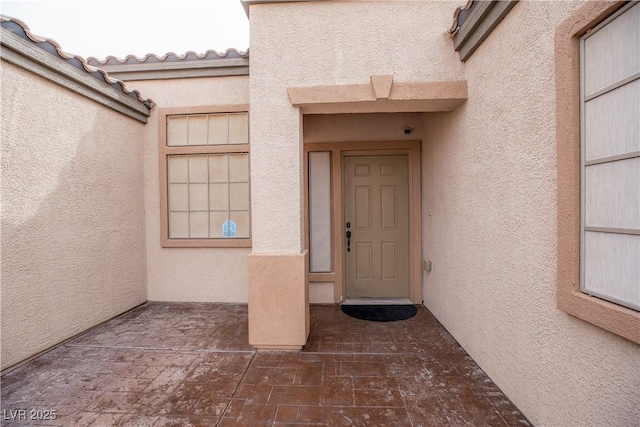 entrance to property featuring a tiled roof and stucco siding