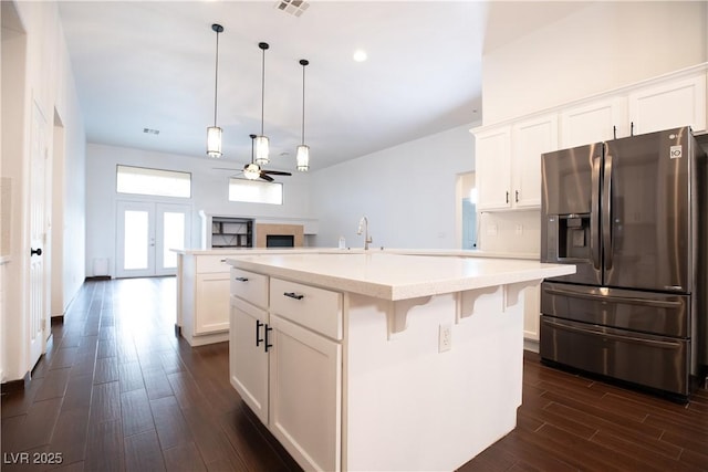 kitchen featuring a center island with sink, stainless steel refrigerator with ice dispenser, dark wood-style floors, white cabinets, and a fireplace