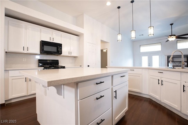 kitchen with dark wood-type flooring, black appliances, a sink, a center island, and ceiling fan