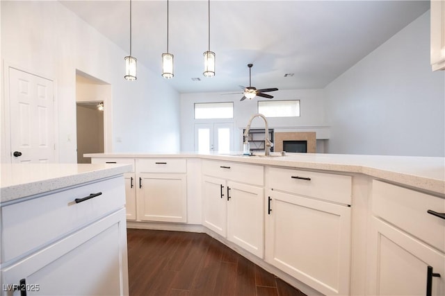 kitchen with a fireplace, dark wood-style floors, white cabinets, a ceiling fan, and a sink