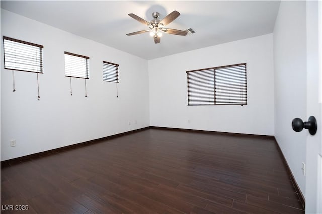 spare room featuring dark wood finished floors, a ceiling fan, visible vents, and baseboards