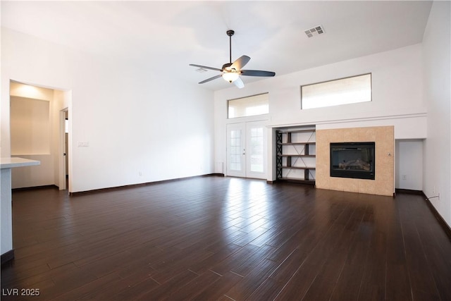 unfurnished living room with visible vents, dark wood-type flooring, baseboards, ceiling fan, and a tiled fireplace