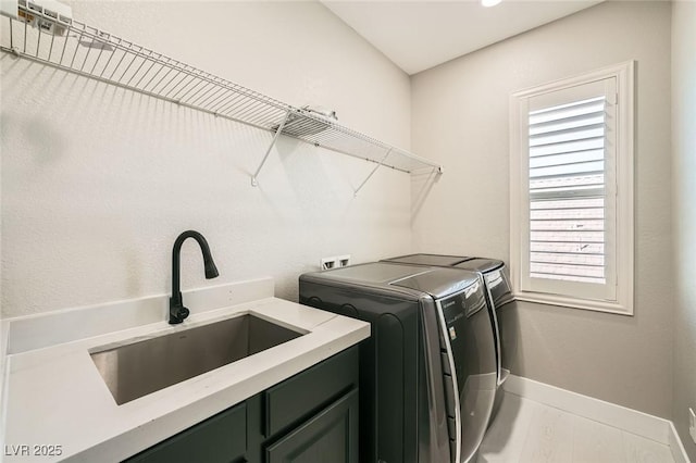 clothes washing area featuring separate washer and dryer, cabinet space, baseboards, and a sink