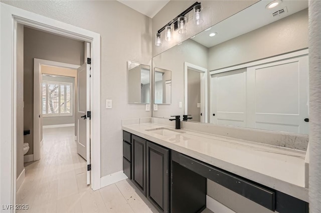 bathroom featuring visible vents, toilet, vanity, and baseboards