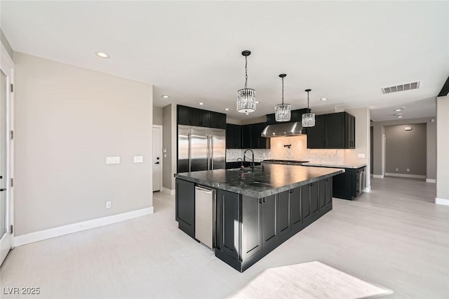 kitchen with dark cabinets, decorative backsplash, visible vents, and built in fridge