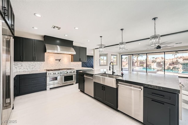 kitchen featuring visible vents, ceiling fan, wall chimney range hood, high quality appliances, and a sink