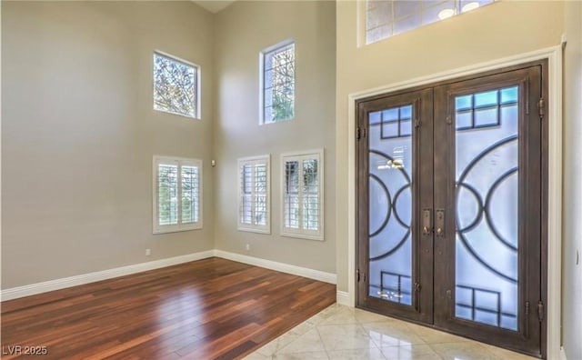 entryway with french doors, baseboards, a high ceiling, and wood finished floors