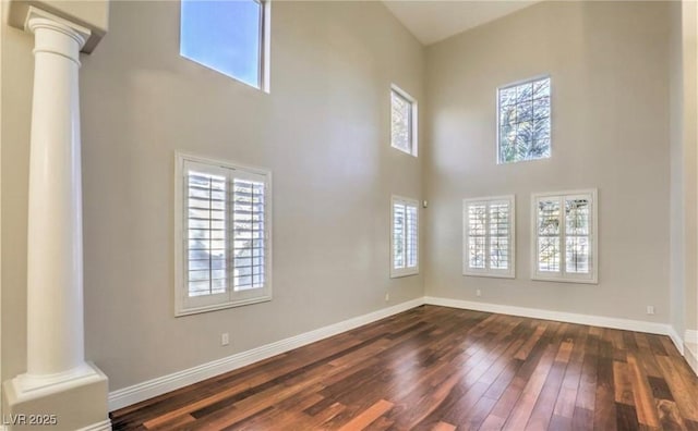 unfurnished living room with decorative columns, baseboards, dark wood-type flooring, and a towering ceiling