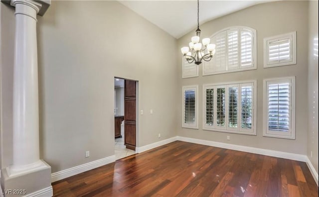 spare room with baseboards, wood finished floors, an inviting chandelier, and decorative columns