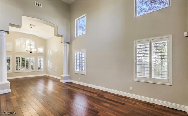 unfurnished living room with a wealth of natural light, visible vents, dark wood-type flooring, and ornate columns