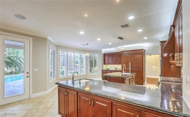 kitchen with visible vents, crown molding, decorative light fixtures, a center island with sink, and a sink