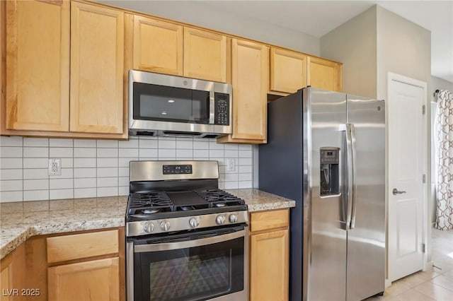 kitchen featuring light brown cabinetry, stainless steel appliances, light stone counters, and tasteful backsplash